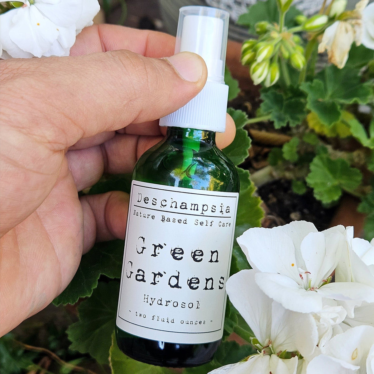Green Gardens Hydrosol bottle held among flowering garden plants