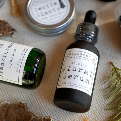 Glowing Floral Serum bottle with dried rose, evergreen sprig, crystals, and botanical materials