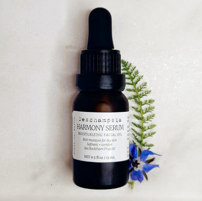 Deschampsia Harmony Serum 15 mL amber dropper bottle beside blue flowers and a fern frond on cream fabric.