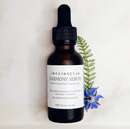 Deschampsia Harmony Serum 30 mL amber dropper bottle beside blue flowers and a fern frond on cream fabric.