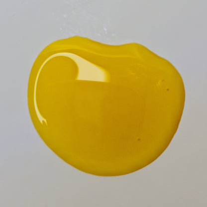 Golden-yellow Harmony Serum facial oil pooled on a pale surface, showing its color and texture.