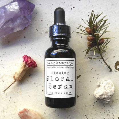 Glowing Floral Serum bottle with dried rose, evergreen sprig, and stones